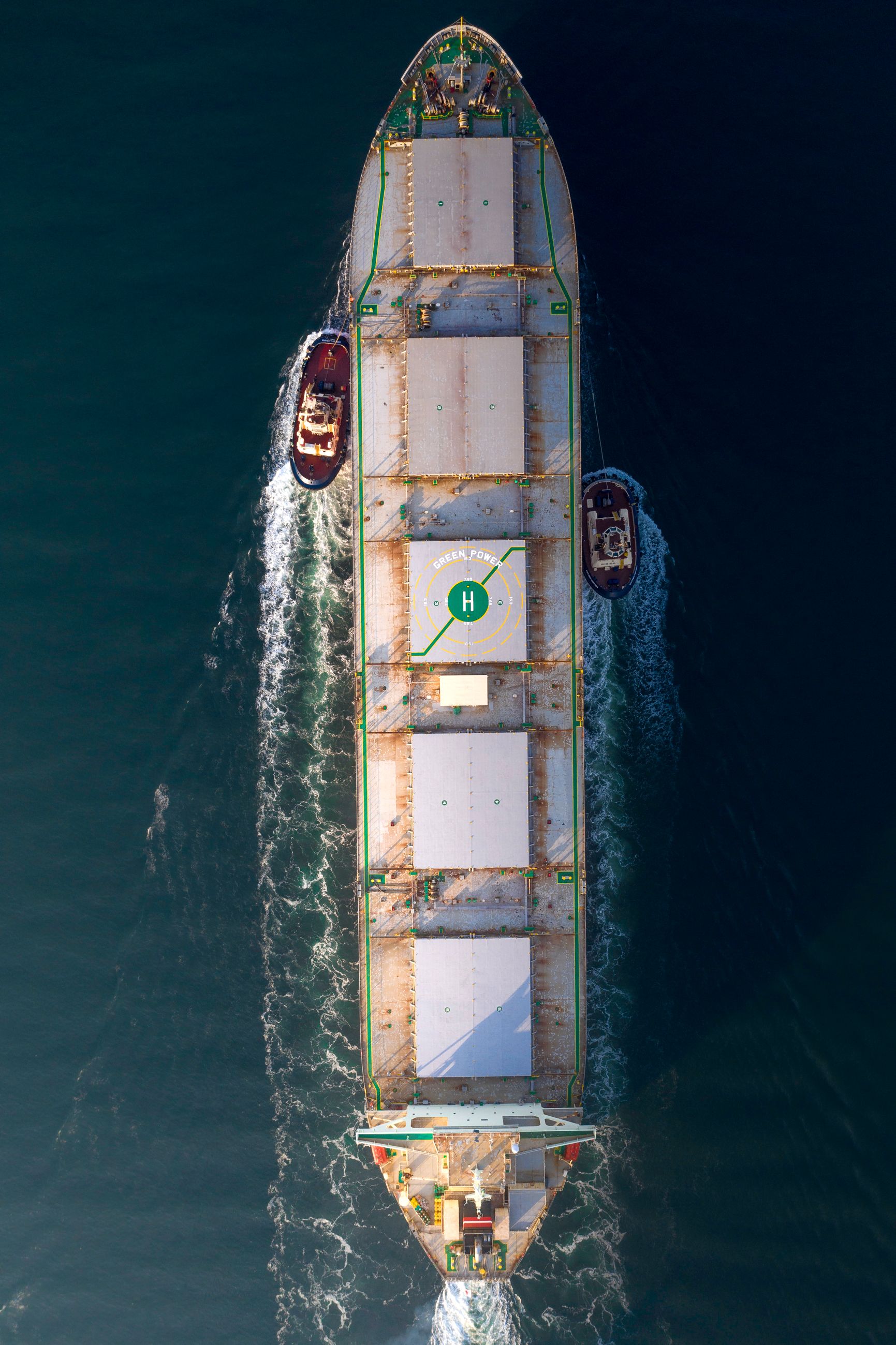 Stillliegendes Containerschiff wird von mehreren Schleppern begleitet
